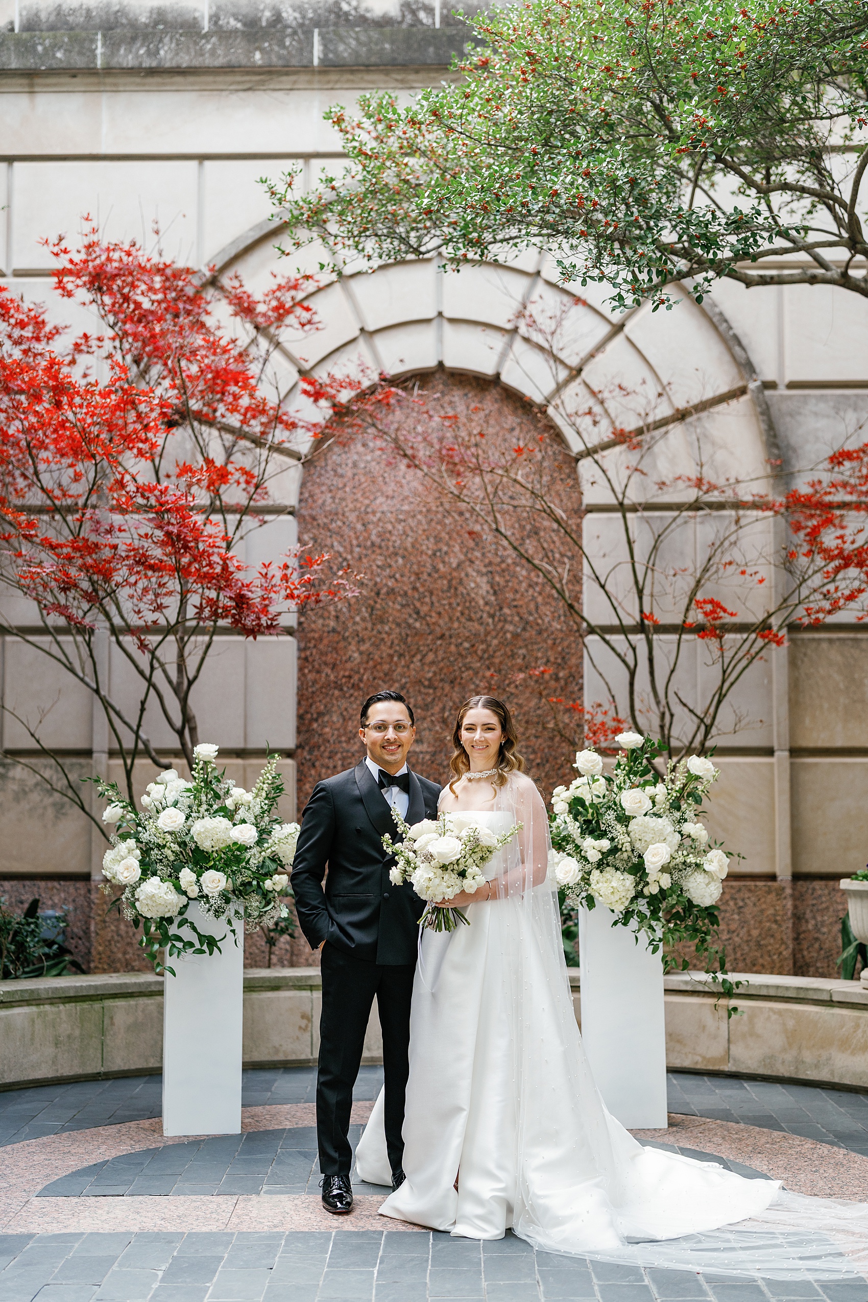 Happy newlyweds stand in front of japanese maples at their Hotel Crescent Court Wedding ceremony