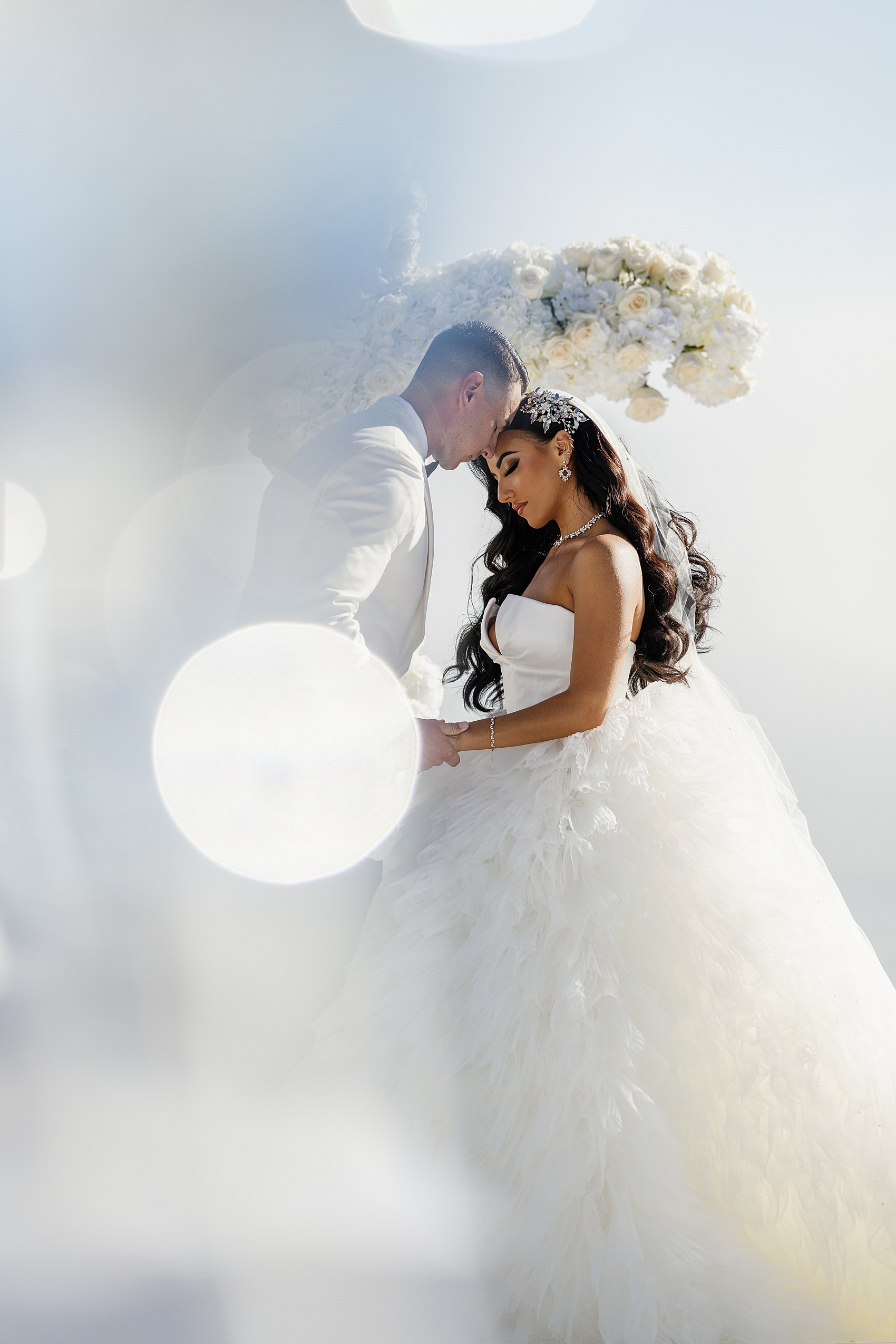 A bride and groom snuggle and hold hands under their white rose cross altar