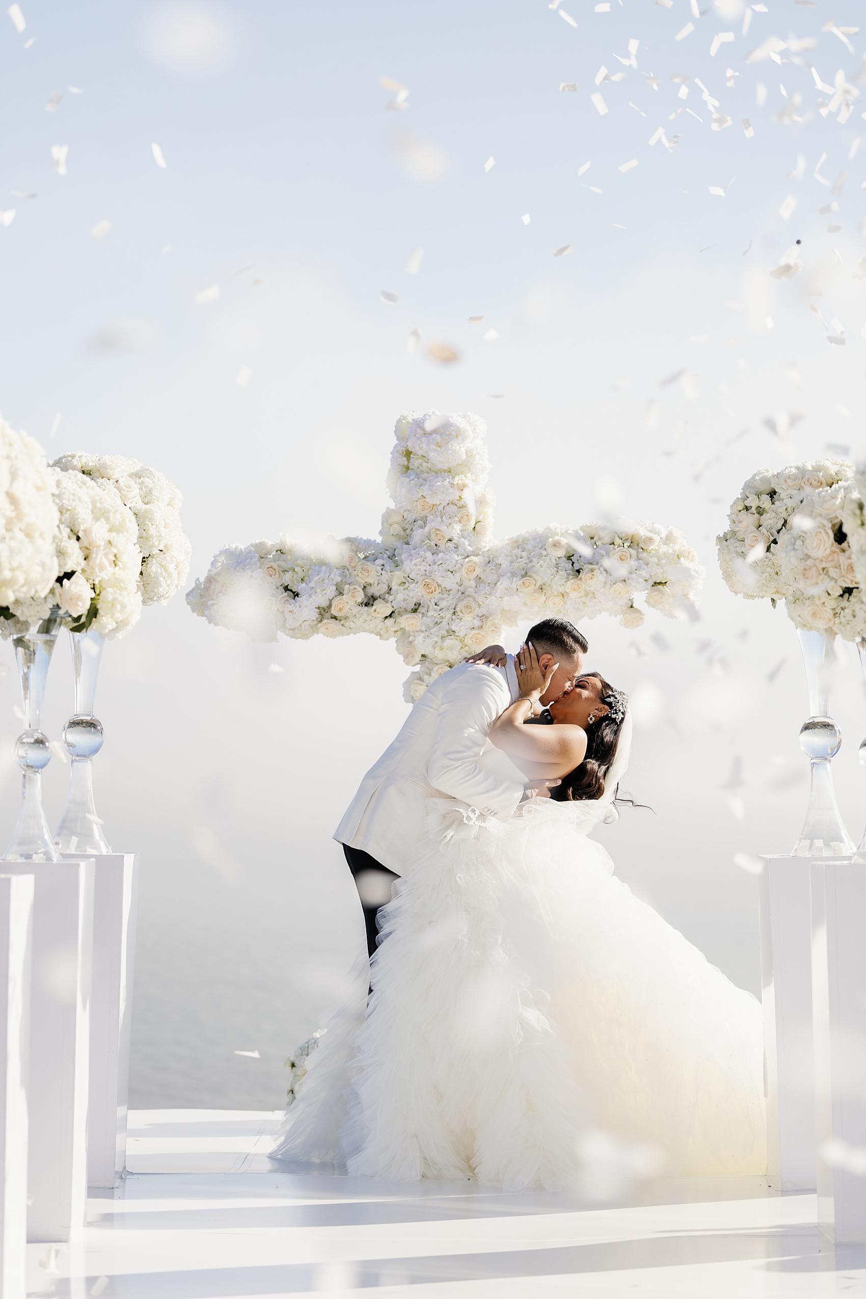 NEwlyweds kiss under falling white rose petals to end their Malibu Sea View Estate wedding ceremony