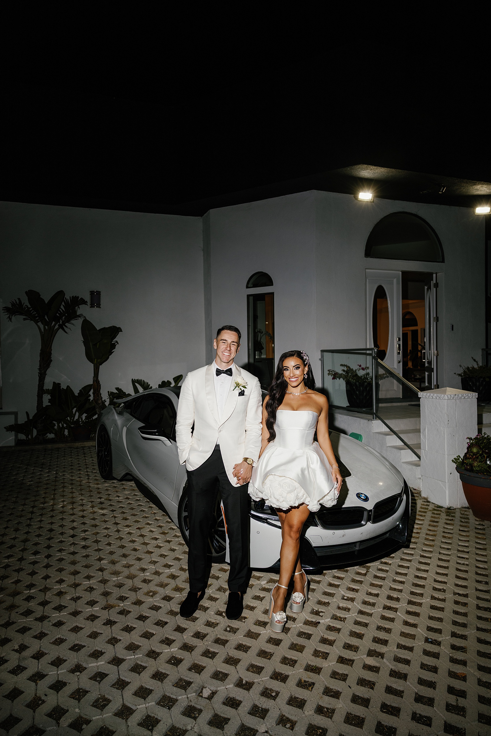Happy newlyweds lean on a BMW and hold hands at night