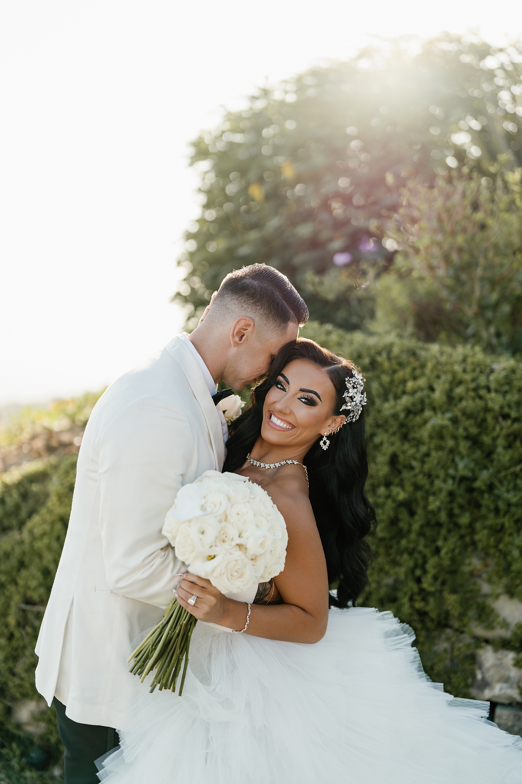A happy bride is hugged and snuggled by her groom in a whtie coat at the Malibu Sea View Estate